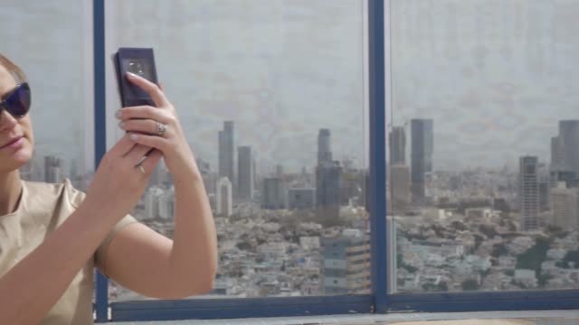 Lächelnde-Frau-macht-Zelle-Foto-gegen-Tel-Aviv-Ansicht-aus-der-Höhe