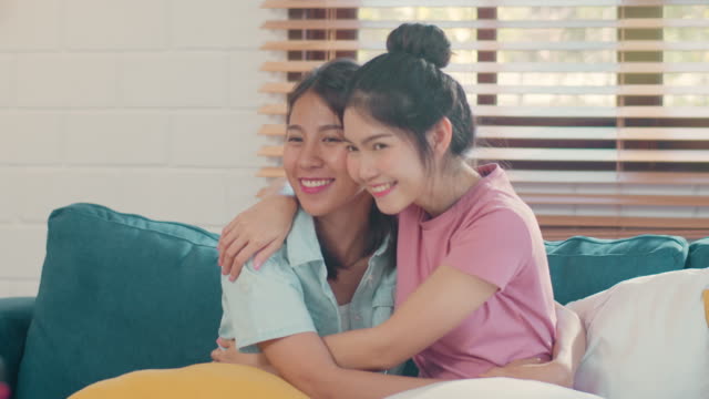Young-Asian-Lesbian-couple-hug-and-kiss-lying-sofa-in-living-room-at-home.