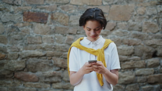 Lächelnde-Teenager-Kind-berühren-Smartphone-Bildschirm-allein-auf-der-Straße-stehend