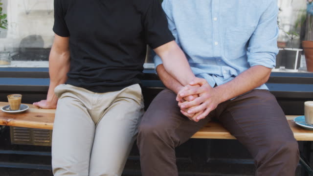 Close-Up-Of-Loving-Male-Gay-Couple-Holding-Hands-Outside-Coffee-Shop