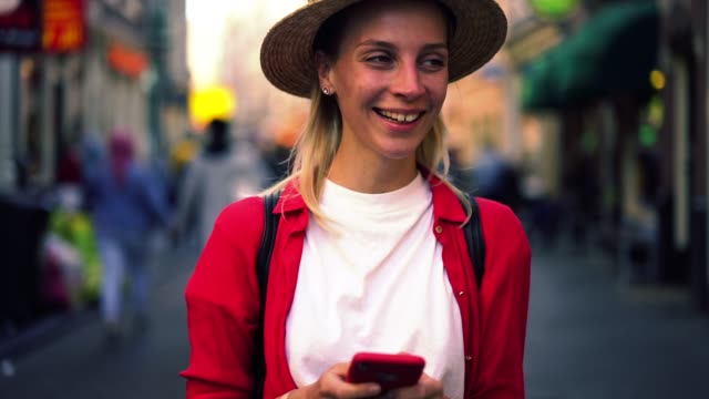 Attractive-caucasian-female-in-red-casual-shirt-typing-text-message-on-mobile-phone-while-standing-outdoors