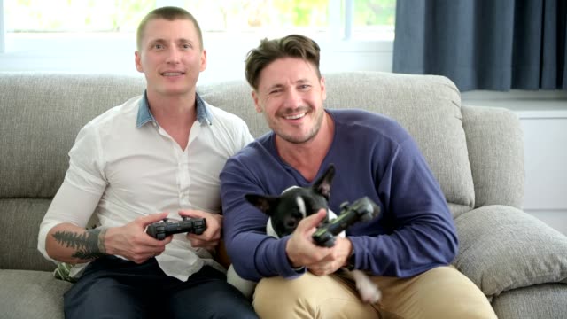 Gay-couple-relaxing-on-couch-with-dog-playing-games.-Very-exciting-mood.