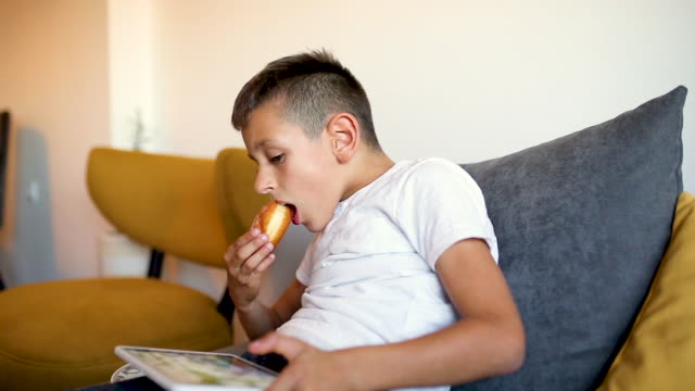 Young-boy-is-playing-games-on-tablet-and-eating-doughnut