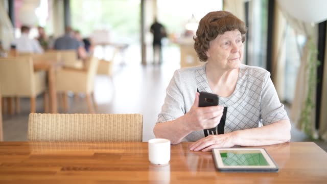 Mujer-mayor-usando-el-teléfono-mientras-piensa-en-la-cafetería
