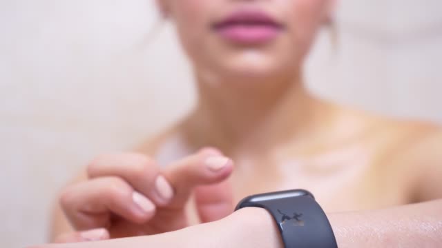 Attractive-young-woman-athlete-wearing-and-using-smartwatch-in-bathroom.-Taping-smartwatch-device-screen.