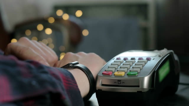 Ein-Mann-bezahlt-in-einem-Café-mit-einer-elektronischen-Smartwatch.-Kontaktlose-Technologie-NFC.-Online-Shopping-mit-moderner-Technologie.-Consumerism-Internet-Online-Käufe.-Mann-zahlt-mit-einer-Smartwatch
