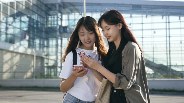 Charmante-junge-asiatische-Mädchen-in-lässiger-Kleidung-mit-Handys-in-der-Nähe-des-Flughafens-stehen