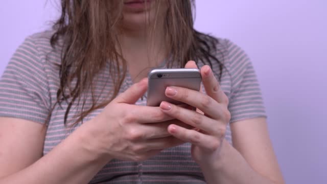 Attraktive-braunhaarige-Mädchen-mit-nassen-Haaren-nutzt-soziale-Netzwerke,-kommuniziert-in-massengers-mit-Freunden-und-Kollegen-per-Smartphone,-aus-nächster-Nähe.-Modernes-Leben-online-mit-Telefon-in-den-Händen-die-ganze-Zeit