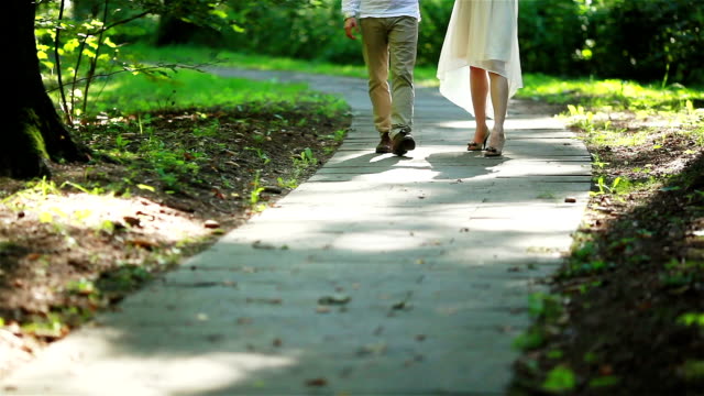 Male-and-female-legs-walking-on-a-path-in-forest-close-up.-Man-and-woman-stepping-onto-sun-lighted-spots-in-spring-park-shallow-depth-of-field.-Togetherness-dating-flirting-marriage-love-story-concept
