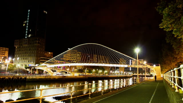 Personas-caminando-en-el-iluminado-puente-de-Zubizuri-de-vidrio-en-el-lapso-de-tiempo,-noche