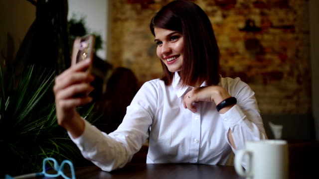 Ein-schönes-Mädchen-sitzt-in-einem-Café-und-nach-einem-heißen-Kaffee-getrunken-stellt-für-eine-Handy-Kamera-zu-einem-schönen-selbst-für-soziale-Netzwerke