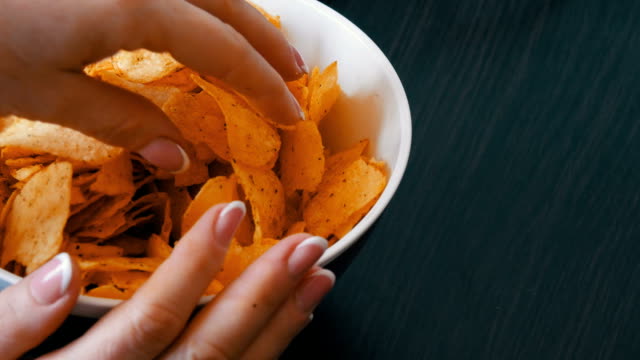 Large-plate-with-potato-chips-on-the-table.-Female-hands-with-beautiful-manicure-take-chips