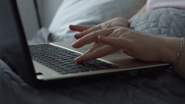 Female-hands-typing-on-laptop-keyboard-in-the-bed