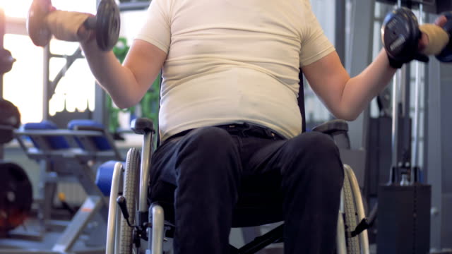 Behinderten-Mann-im-Rollstuhl-mit-Hantel-in-ein-Fitness-Studio-trainieren.