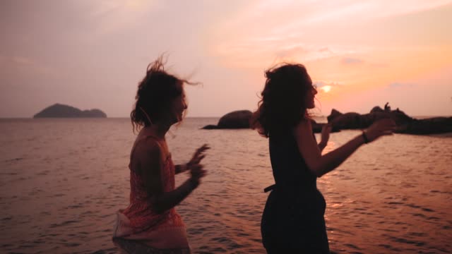 zwei-glückliche-Mädchen-tanzen-am-Strand-bei-Sonnenuntergang-in-Zeitlupe