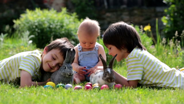 Niños-lindos,-hermanos-niño,-niño-y-preescolar,-jugando-con-conejitos-y-huevos-de-Pascua-en-una-primavera-floreciente-jardín.-Niño-juega-con-el-conejo,-caza-para-vacaciones-del-huevo