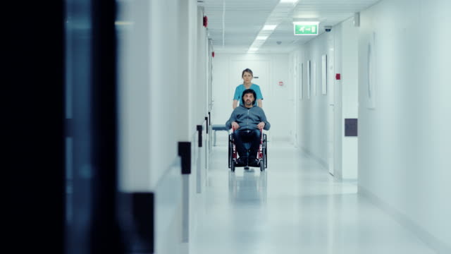 Mujer-enfermera-empujar-el-paciente-en-la-silla-de-ruedas-a-través-del-Hospital,-que-van-a-los-procedimientos.-Brillante-moderno-Hospital-con-un-personal-amable.