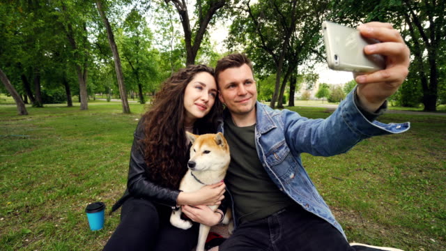 Fröhlicher-Kerl-nimmt-Selfie-holding-Smartphone-und-seine-Frau-zu-küssen,-während-sie-entzückenden-Hund-hält-und-küssen.-Beziehung,-Liebe,-Romantik-und-Technologie-Konzept.