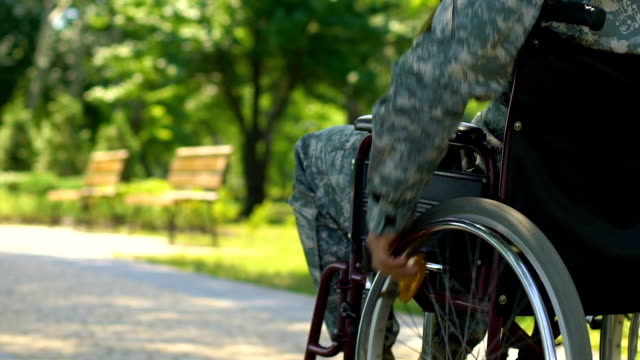 Veterano-de-la-guerra-en-silla-de-ruedas-moviendo-lentamente-a-lo-largo-del-parque,-defensor-del-país-de-héroe