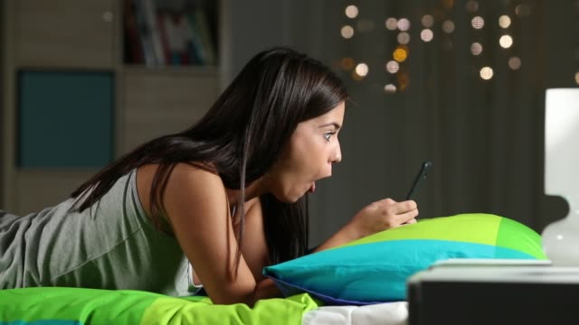 Überrascht-Teen-beobachten-Medien-in-einem-Telefon-auf-einem-Bett