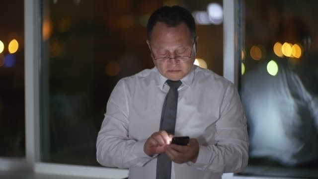 Asian-White-Collar-Worker-Using-Smartphone-in-Dark-Office
