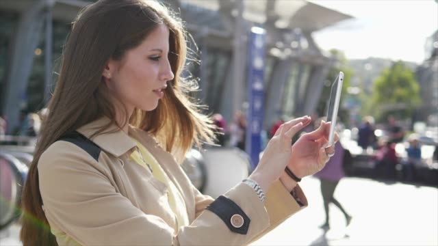 Gut-aussehende-junge-Frau,-die-auf-digitale-Tablet-im-öffentlichen-Raum-außerhalb-arbeiten