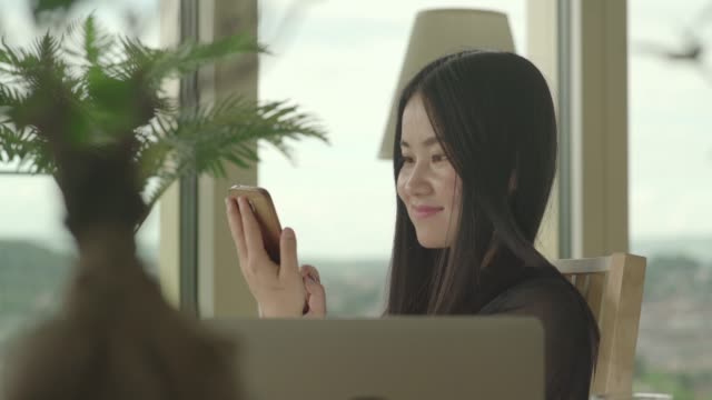 Mujer-asiática-joven-sentado-en-casa-y-golpes-fuertes-en-la-pantalla-táctil-del-teléfono-inteligente