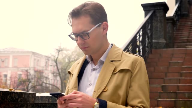 Closeup-of-attractive-caucasian-male-typing-on-the-phone-calmly-standing-in-the-park-outdoors