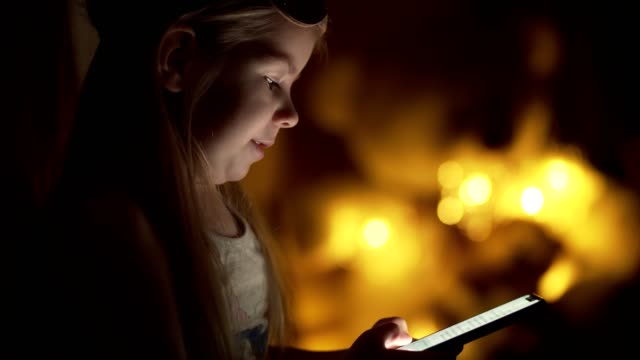 Little-girl-typing-message.-Child-at-night-uses-smartphone-with-copyspace