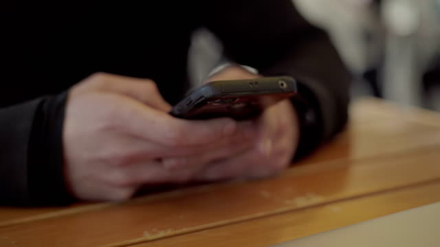 Male-hands-using-smartphone-above-wooden-table