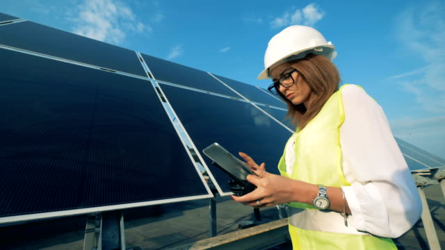 Woman-types-on-a-tablet-while-working-near-solar-panels,-close-up.