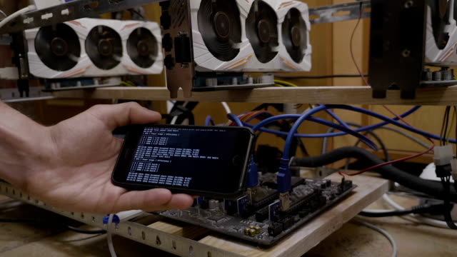 Business-young-man-hand-holding-phone-with-miner-app-running-close-to-gpu-ethereum-mining-rig