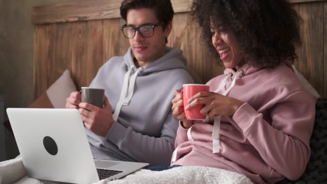 Couple-drinking-coffee-and-using-laptop-in-bed
