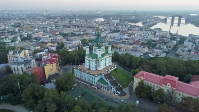 Vista-aérea-de-la-iglesia-de-San-Andrés-y-el-distrito-de-Podil-en-el-río-Dnieper-antes-de-la-puesta-del-sol-en-Kiev,-Ucrania.-4K,-UHD