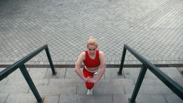 Plus-size-mixed-race-blonde-smiling-woman-wearing-red-sportswear-warm-up-before-run