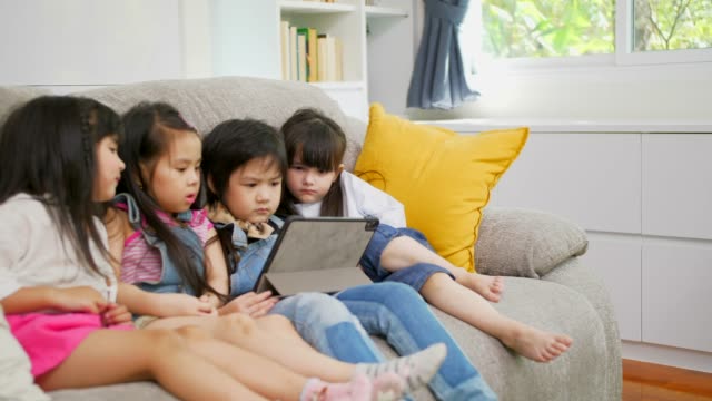 Gruppe-von-Kindern,-die-mit-digitalem-Tablet-zusammen-auf-dem-Sofa-zu-Hause-spielen,-und-lächelnd,-Kinder-auf-digitalem-Tablet-im-Wohnzimmer.