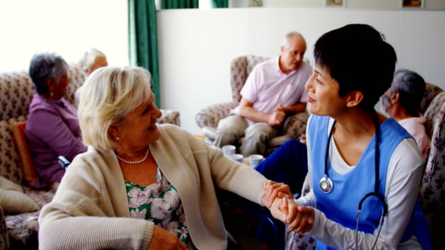 Vista-frontal-del-médico-asiático-que-interactúa-con-la-mujer-mayor-en-el-hogar-de-ancianos-4k