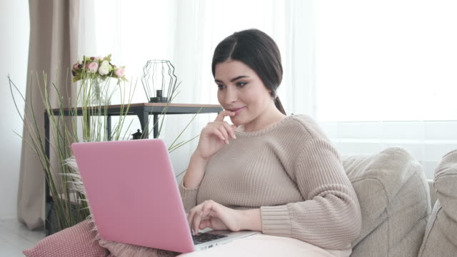 Happy-woman-with-laptop-on-sofa
