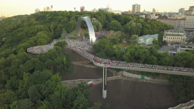 Eine-Menschenmenge-auf-einer-Fußgängerbrücke-ist-am-Frühlingsabend-zu-sehen.-Luftaufnahme.-Eine-neue-Fahrrad-Fußgängerbrücke-im-Zentrum-der-Hauptstadt-der-Ukraine,-der-Stadt-Kiew.-Ausflüge-und-Spaziergänge-für-Touristen