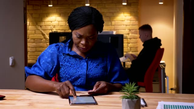 Nahaufnahme-von-erwachsenen-afrikanischen-amerikanischen-Geschäftsfrau-SMS-auf-dem-Tablet-im-Büro-drinnen-am-Arbeitsplatz