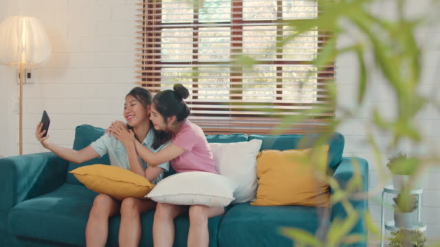 Junge-asiatische-lesbische-Paar-mit-Handy-Selfie,-während-liegen-Sofa-im-Wohnzimmer-zu-Hause.