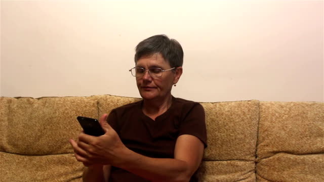 Attraktive-erwachsene-Frau-lesen-einen-News-Feed-auf-einem-Smartphone,-während-auf-einem-Sofa-zu-Hause-sitzen.