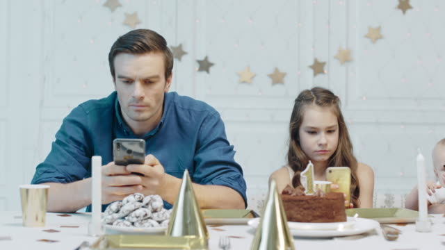 Serious-father-and-daughter-holding-mobile-cellphones-on-festive-table.