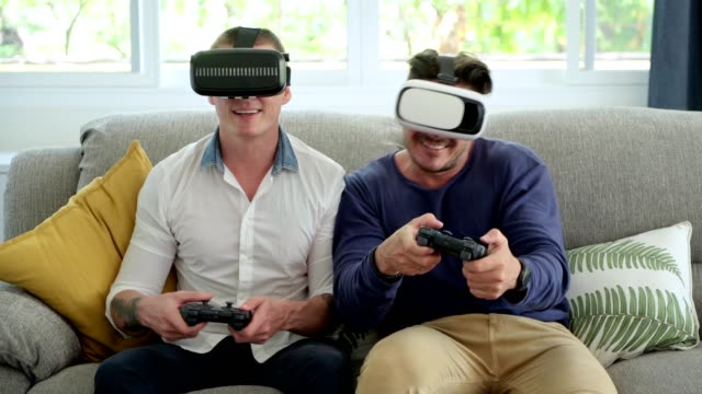 Pareja-gay-relajándose-en-el-sofá-jugando-juegos-de-realidad-virtual.-Juego-de-la-competencia.