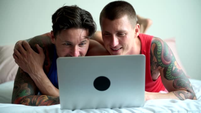 Schwules-Paar-im-Bett-mit-Laptop-Computer.-Kopfnicken.