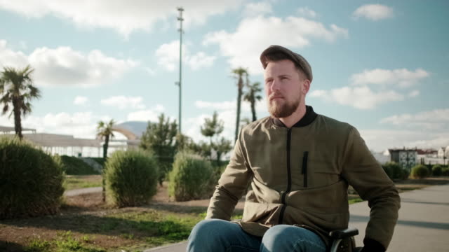Confident-bearded-man-is-riding-on-wheelchair-outdoors-alone-in-sunny-day