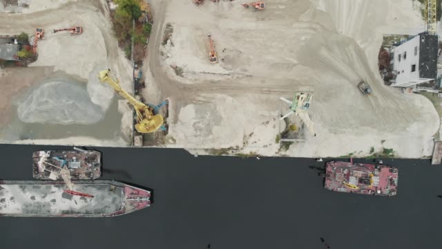 Hafenkräne-am-Flussufer-produzieren-Sand.-Hafenkräne-mit-einem-Eimer-am-Flussufer.-Sandabbau-mit-Lkw-und-Baggern