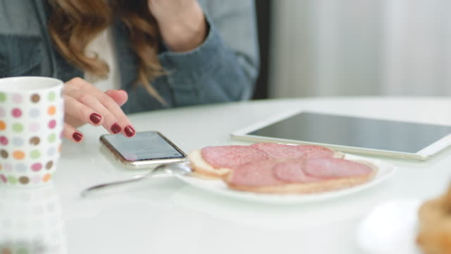 Closeup-female-hands-scrolling-mobile-phone-while-eating-sandwich