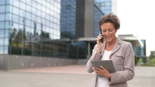 Glückliche-reife-Geschäftsfrau-mit-Telefon-und-digitale-Tablet-in-der-Stadt-im-Freien