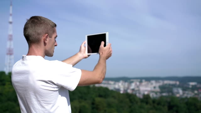 attraktiver-junger-Mann-fängt-das-umliegende-Panorama-auf-einem-Tablet-ein